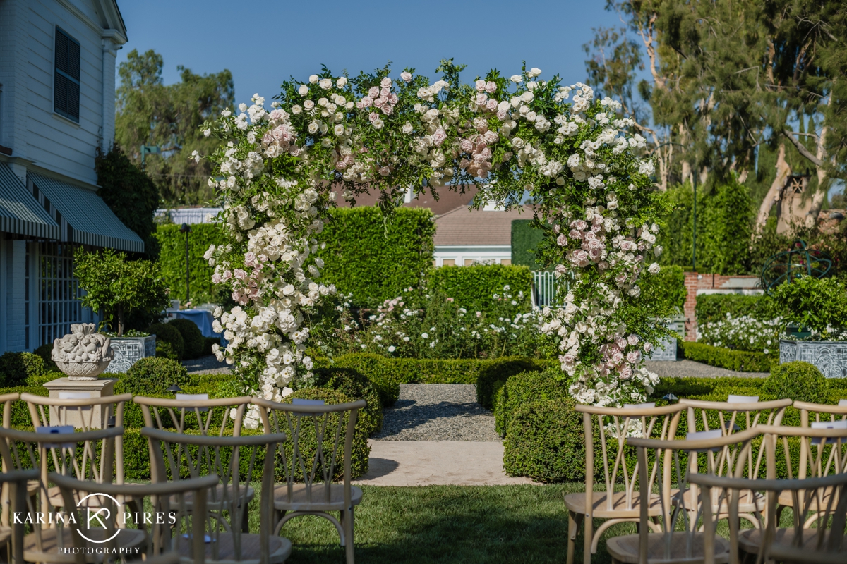 Greenery arch with white and blush roses at an outdoor wedding ceremony in California