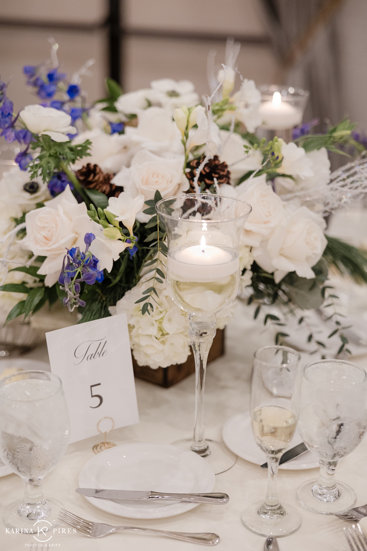 Winter wedding centerpiece filled with white and dark blue flowers and pinecones
