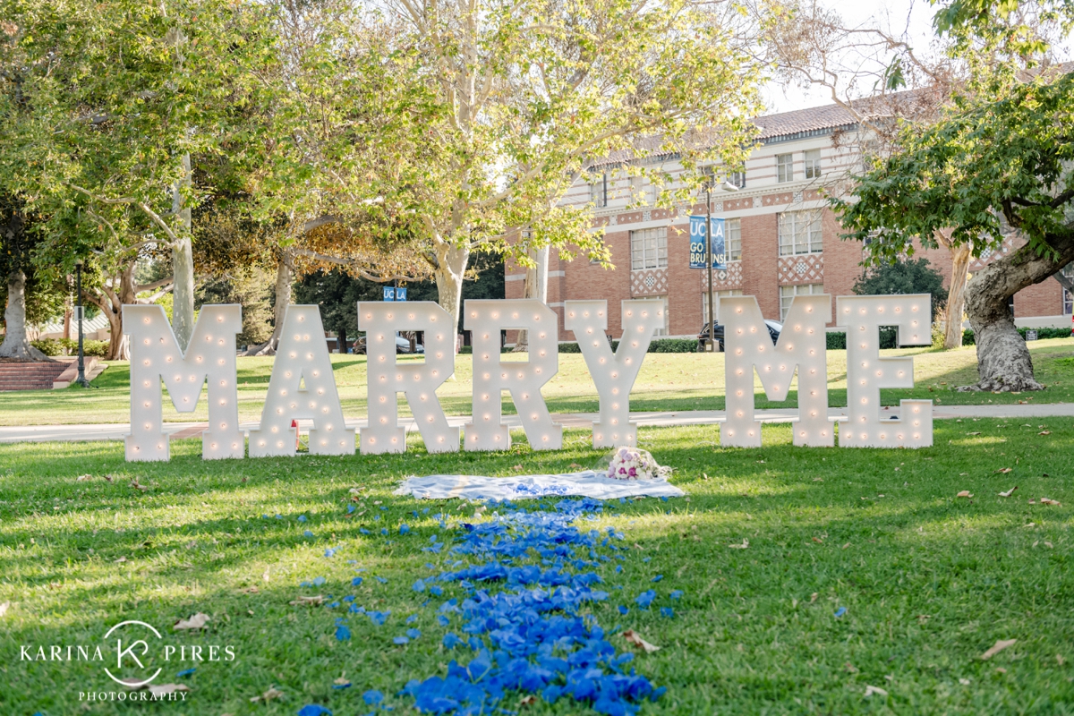 Surprise proposal at UCLA, featuring a glowing ‘Marry Me’ sign surrounded by rose petals and candles.