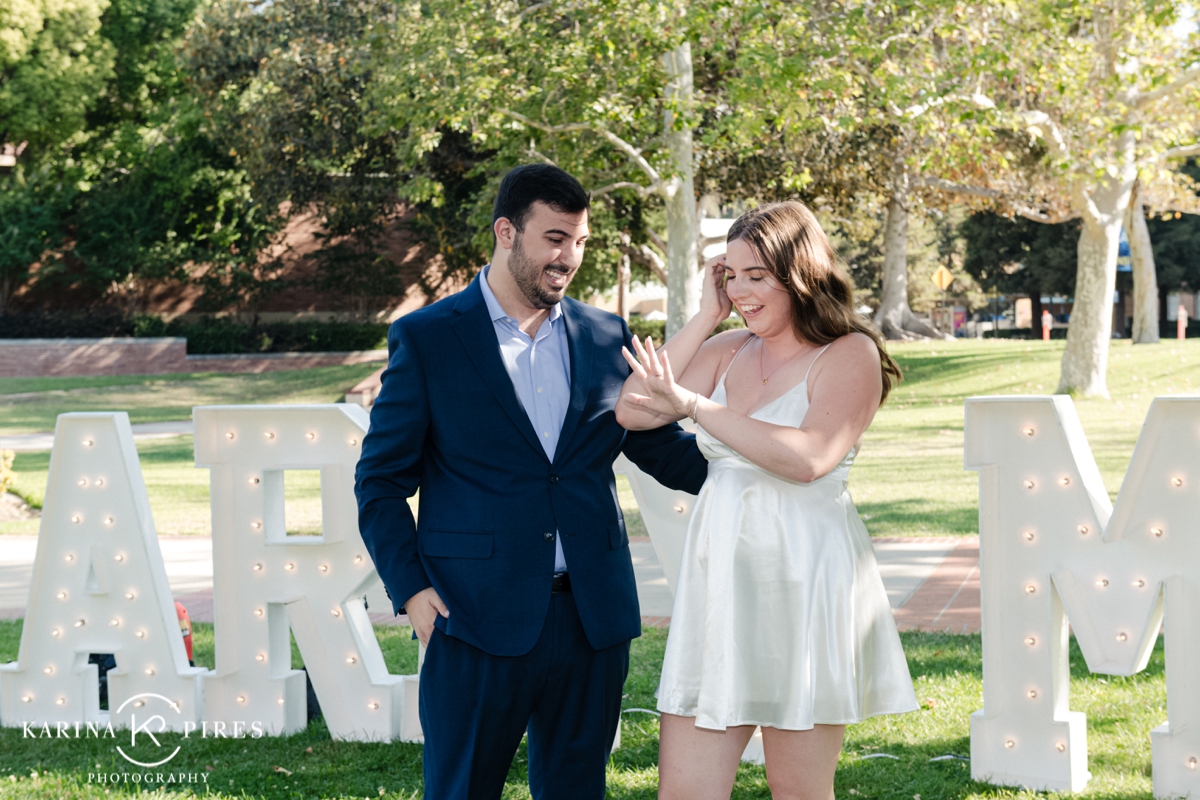 Man on one knee proposing to his fiance in front of a ‘Marry Me’ sign at UCLA