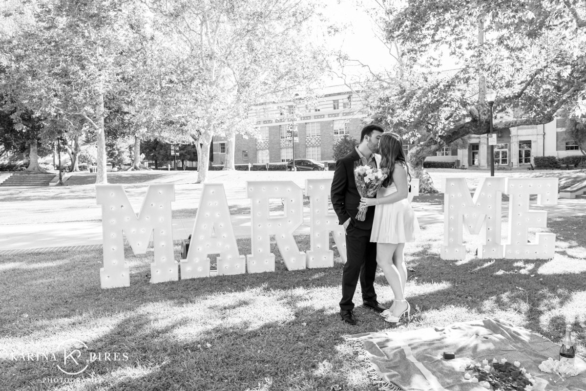 Surprise proposal at UCLA, featuring a glowing ‘Marry Me’ sign surrounded by rose petals and candles.