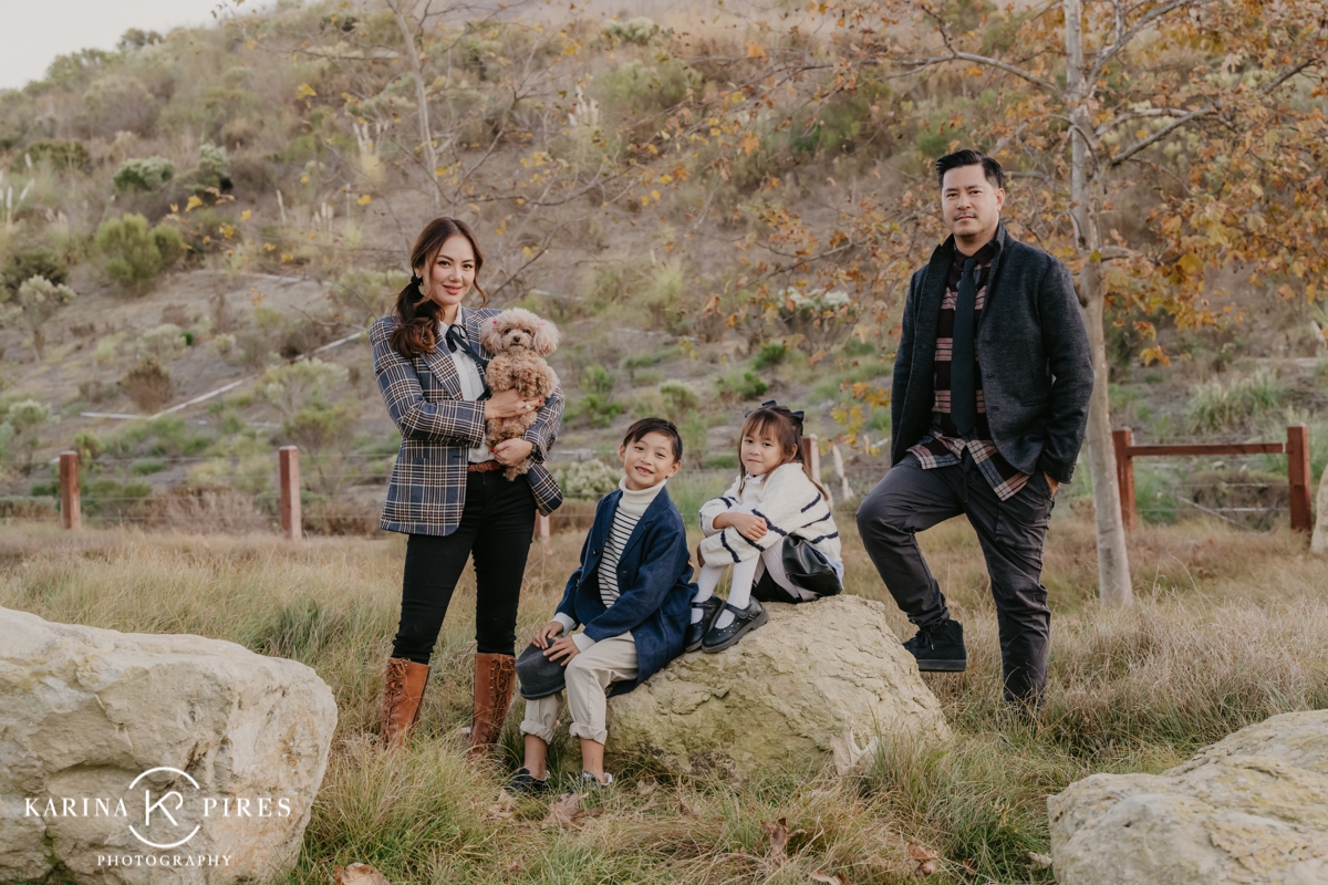 Family posing outdoors in Irvine, California, surrounded by vibrant fall leaves during a playful and candid session.