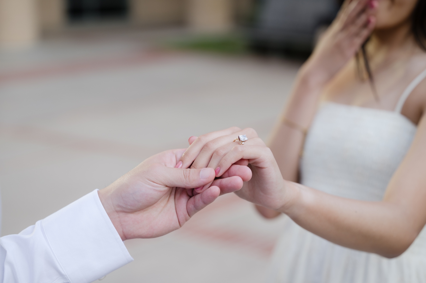 Detail of man holding a brides hand, with her wearing an emerald engagement ring