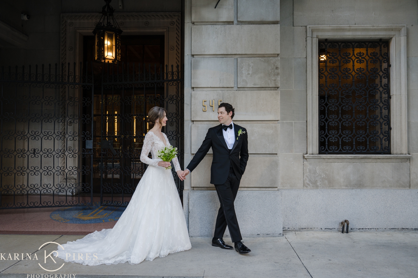 A wedding holding hands and walking along the sidewalk outside the Jonathan Club's historic facade on West Sixth Street in Downtown Los Angeles