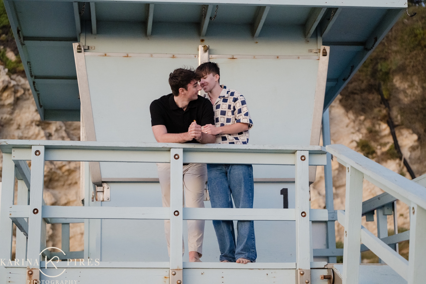 Dustin and Caleb kissing beside an iconic Los Angeles lifeguard tower at sunset, for their proposal session